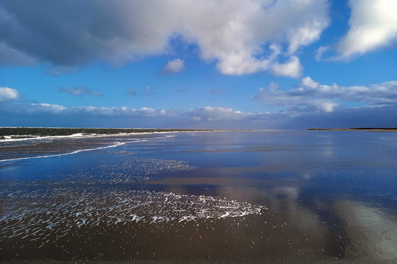 strand met weerspiegeling blauwe lucht en witte wolken