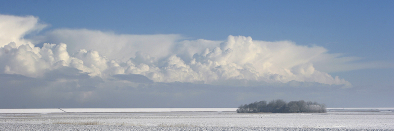 sneeuw met grote witte wolken boven waddenboerderij